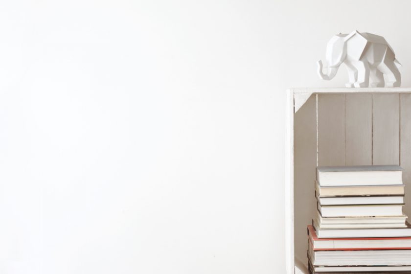 minimalist books stacked in white crate with white elephant on white wall