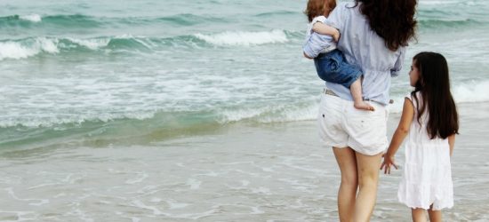 homeschool mom with young daughter and baby walking in the waves on the beach