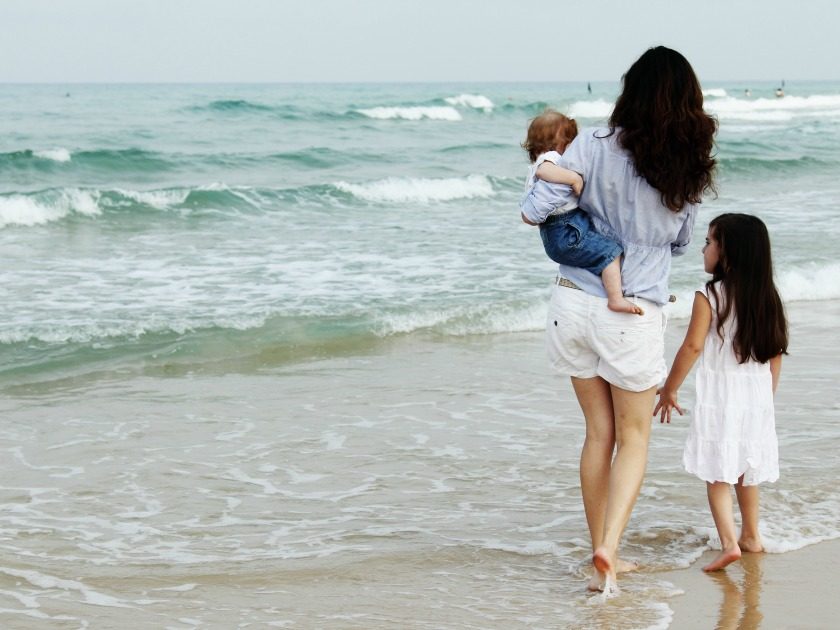 homeschool mom with young daughter and baby walking in the waves on the beach
