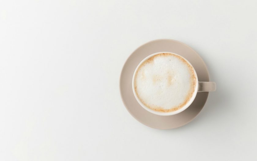 latte with foam in minimalist light brown coffee cup on plain white background