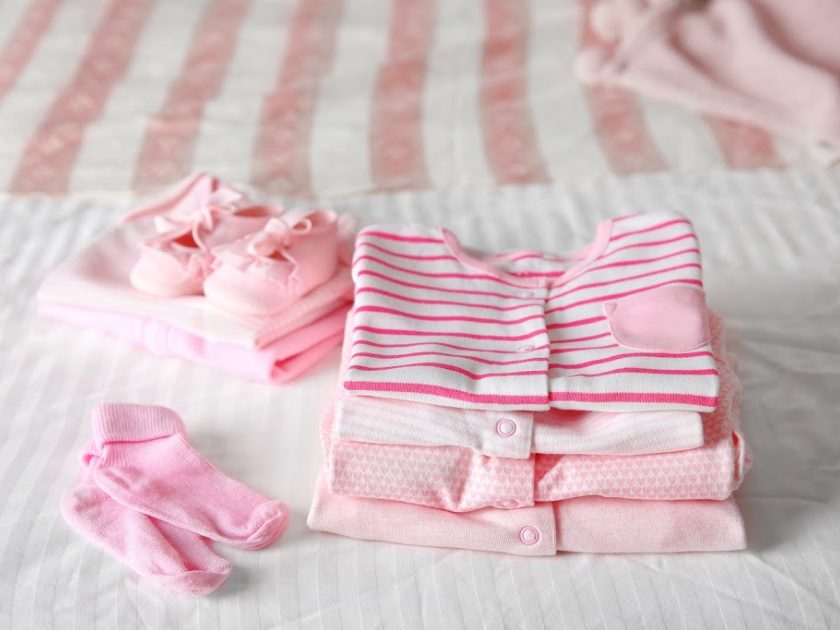 folded pink and white baby clothes on made bed