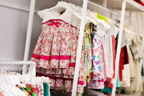 dozens of baby dresses not folded, on hangers on long rack instead