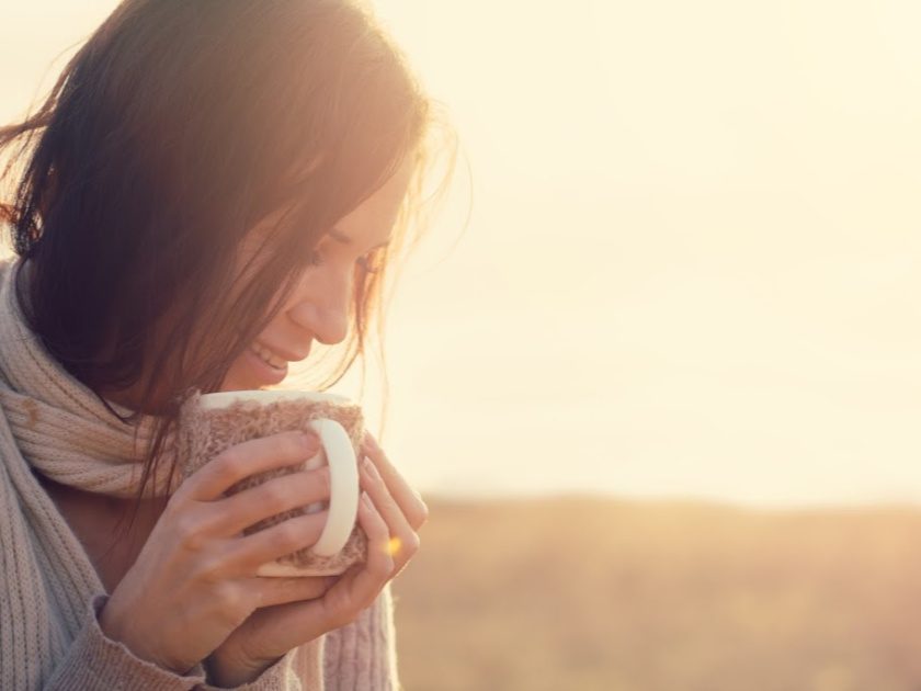 happy minimalist mom wearing scarf with coffee mug outside in sunlight