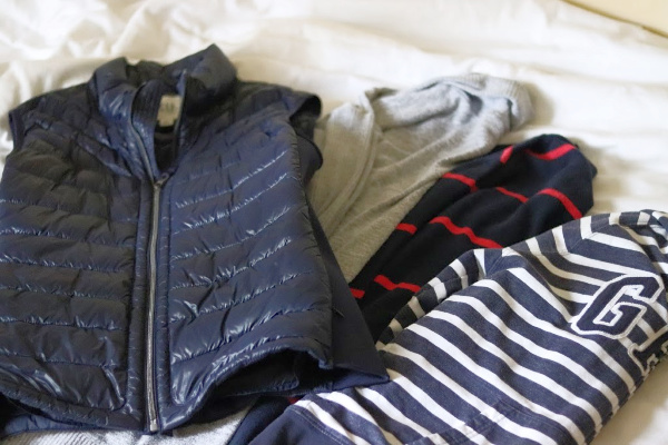 blue vest, grey and blue sweaters and sweatshirts for fall on white bedspread