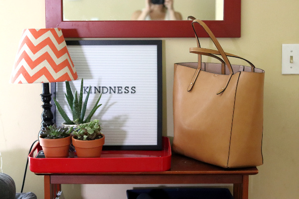 light brown tote on shelf with orange, white and black lamp, succulents and letterboard that says "kindness"