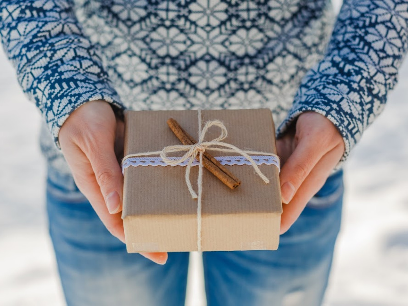 hands holding a gift wrapped in brown kraft paper, tied with twine, lace and a cinnamon stick