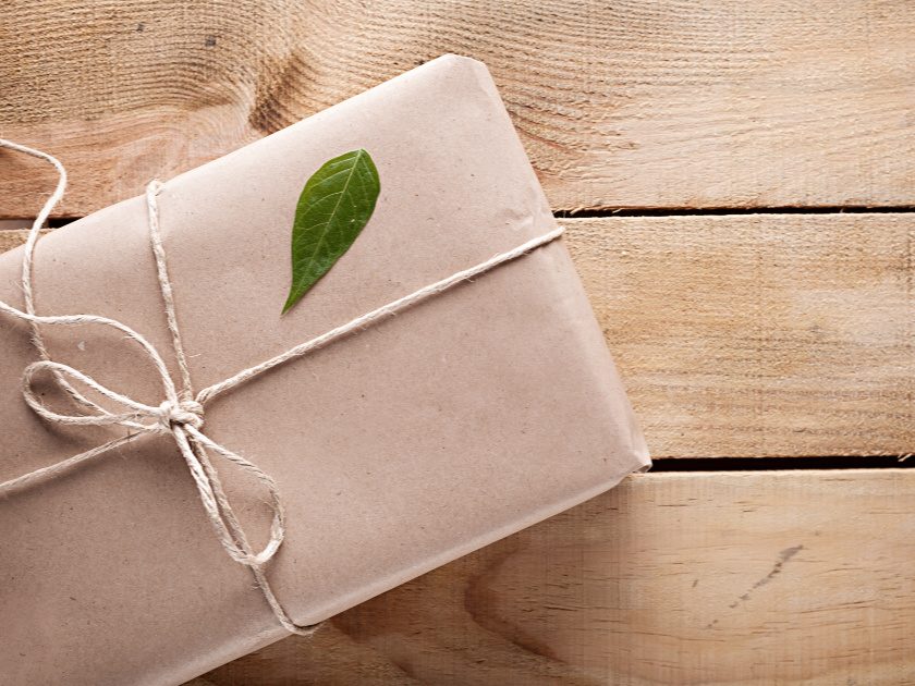 minimalist gift box in brown kraft paper with a green leaf on it on wooden background