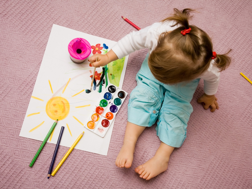 toddler with pigtails painting with watercolors while sitting on patterned blanket