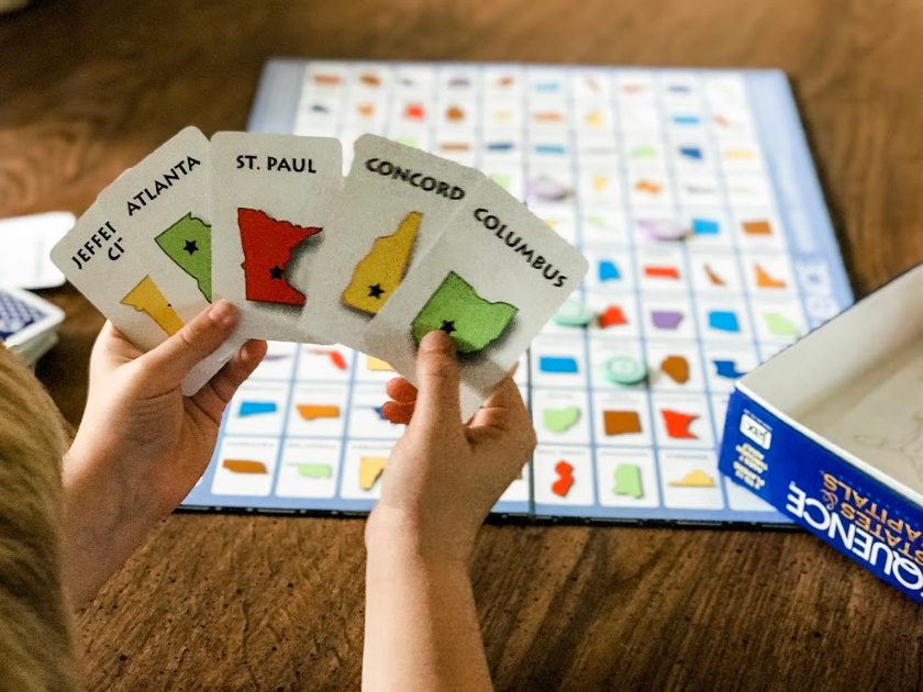 young boy playing Sequence states and capitals board game, holding up cards in his hand