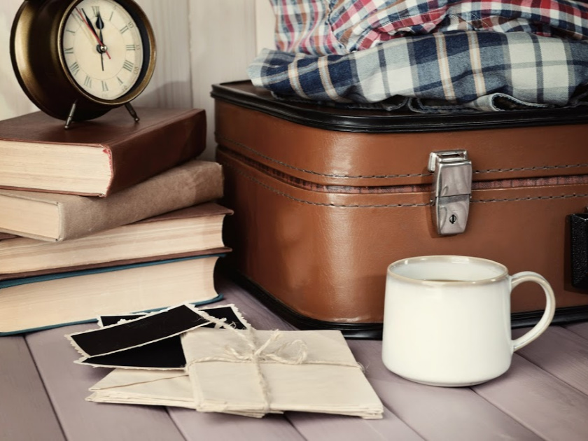 stack of old books with alarm clock on top, old suitcase with flannel shirts, old photographs tied in twine and white mug