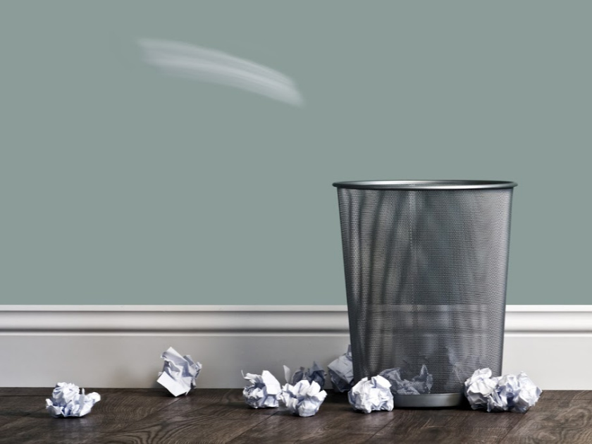 metal wastebasket surrounded by crumpled pieces of paper