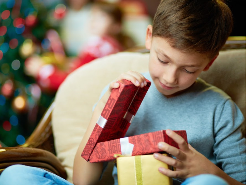 little boy opening lid of red present, Christmas tree in background
