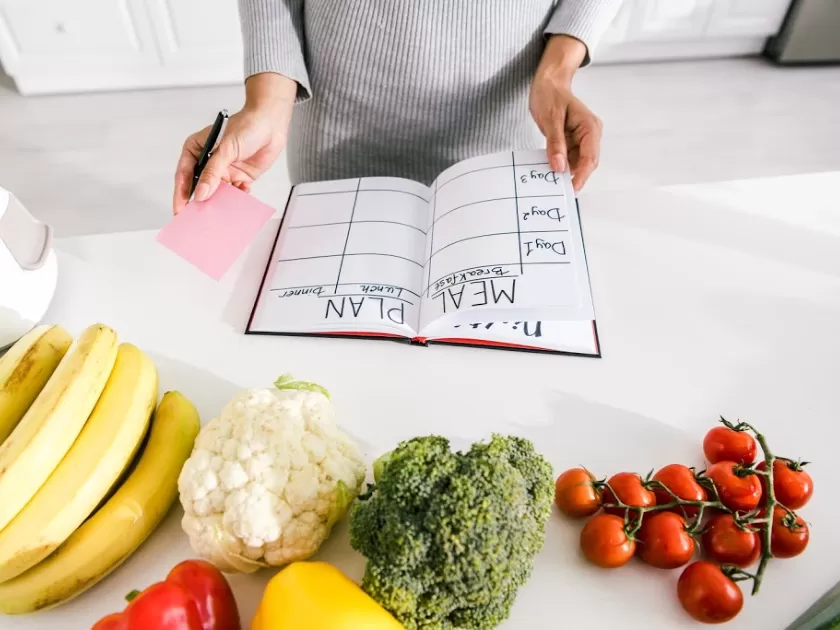 woman meal planning with book on counter, surrounded by fruits and veggies