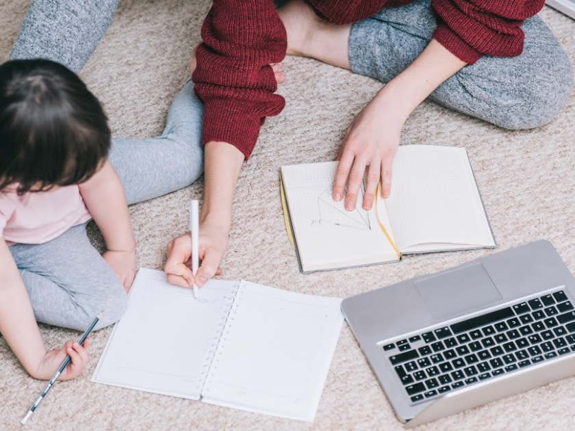 mom sitting next to small child on the floor, her computer in front of her, working while helping with homeschool work