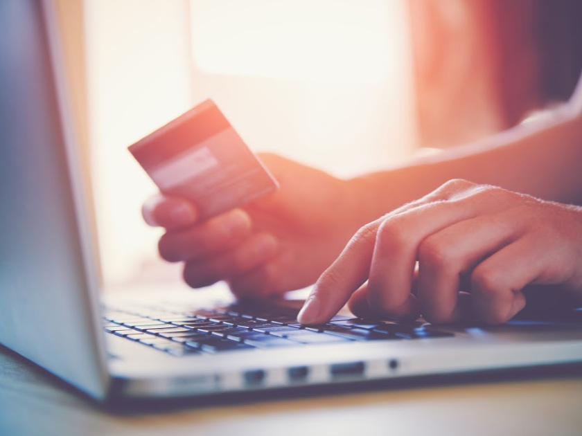 person holding credit card, trying to buy clothes on a laptop