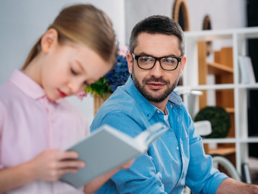 homeschool dad looking at daughter reading book