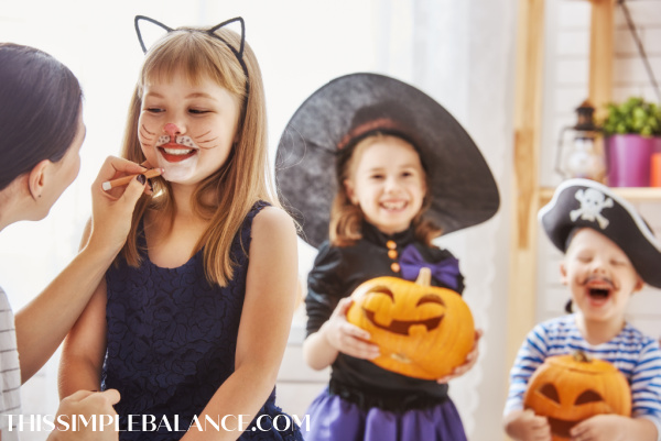 little kids dressed up for Halloween with mom painting cat makeup on little girl