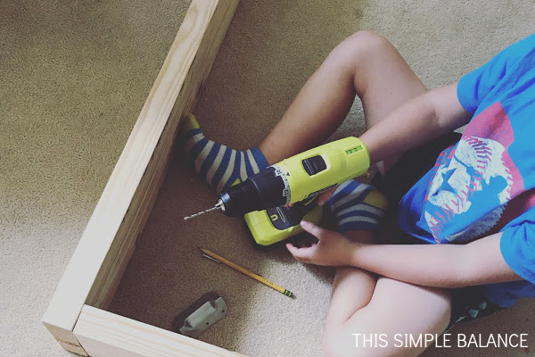 older boy holding drill constructing raised planter beds