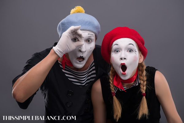 two mimes with faces painted white, wearing berets and making surprised faces