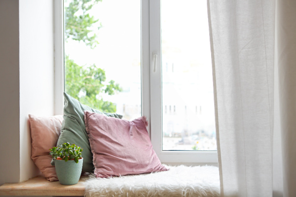 window ledge with three pastel-colored throw pillows, white cozy rug and house plant