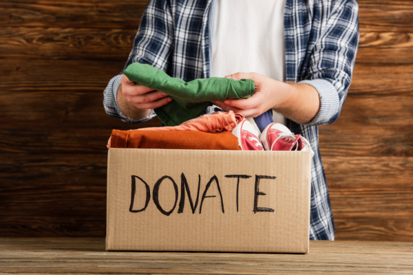 man folding clothes and putting them in a cardboard box labeled "donate"