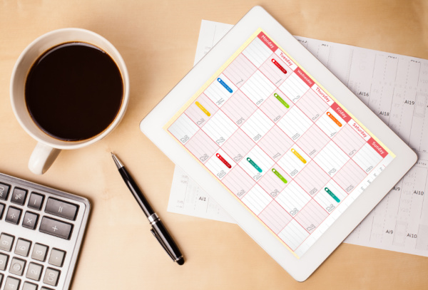 colorful calendar on white tablet on desk with coffee and pen