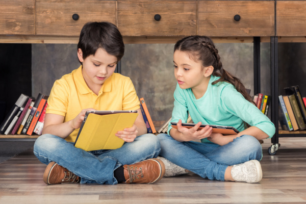 two kids sitting next to each other on the floor using tablets