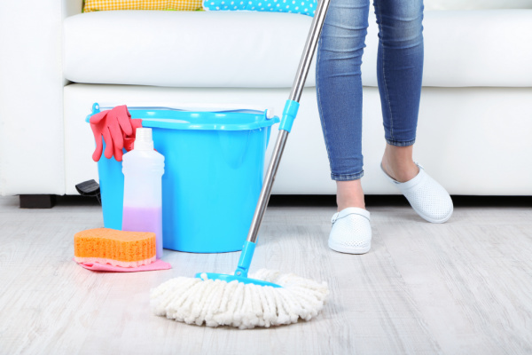 mom in jeans and white clogs mopping, with cleaning bucket and supplies nearby