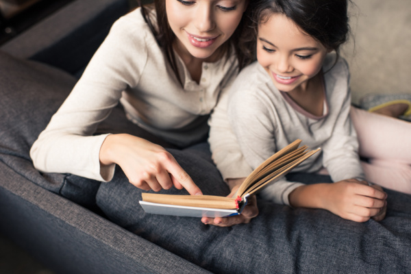 mom and daughter snuggled on gray couch reading book together