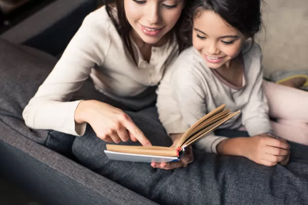 mom and daughter snuggled on gray couch reading book together