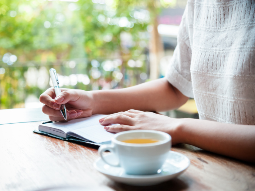 woman sitting at table with tea and journal, writing