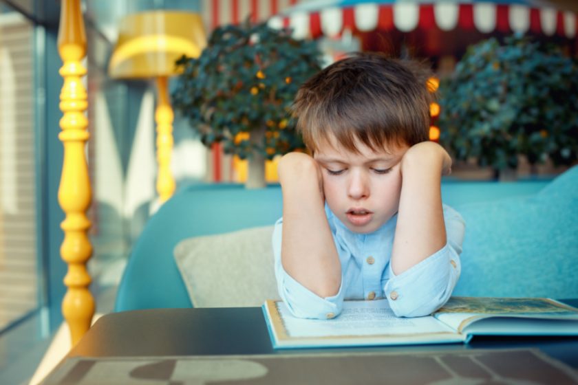 young boy with elbows on book on table reading