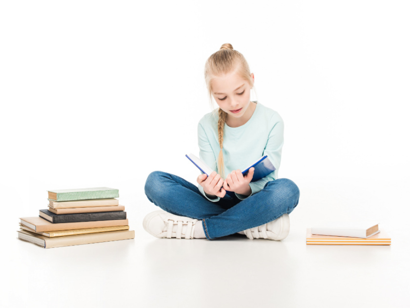 girl reading books with stacks of books beside her