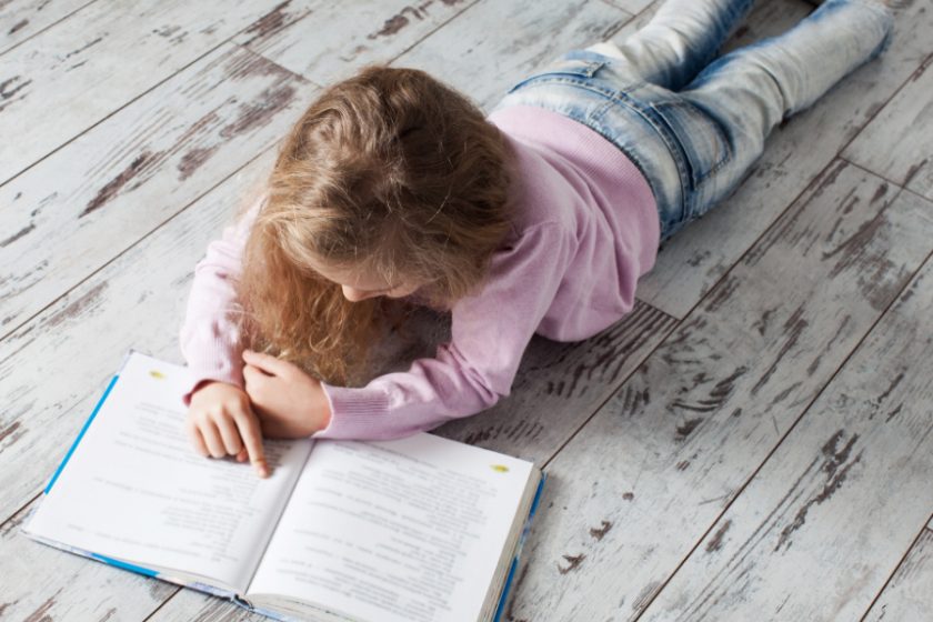 young girl laying on floor reading a book