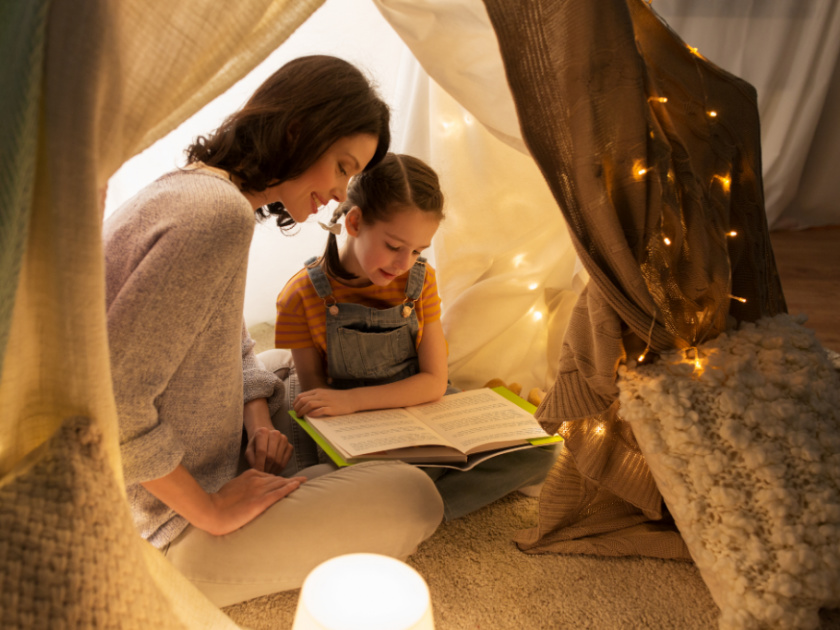 mom reading daughter picture books about immigration while sitting in a tent with sparkle lights