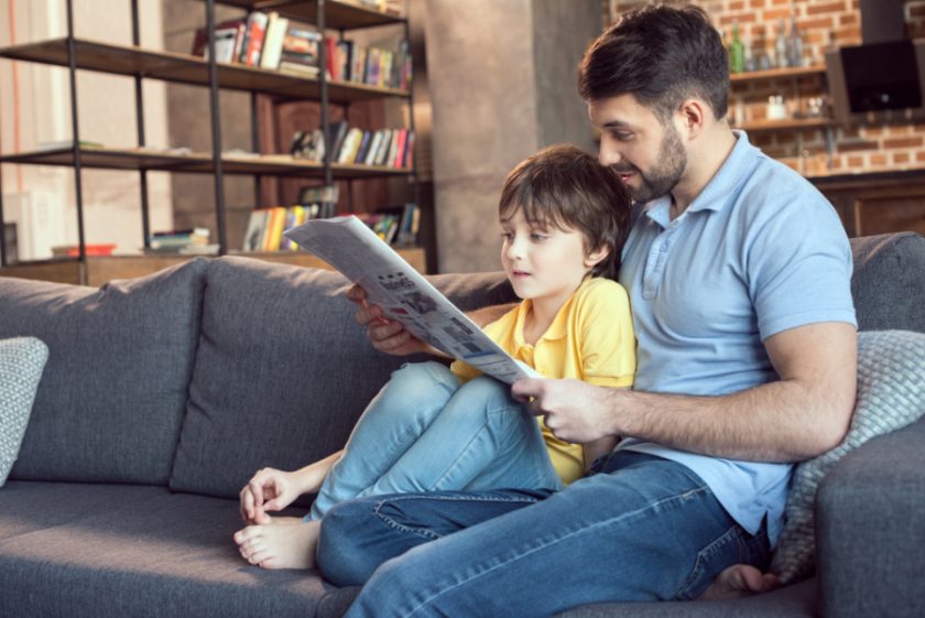 father and son sitting together on couch reading newspaper