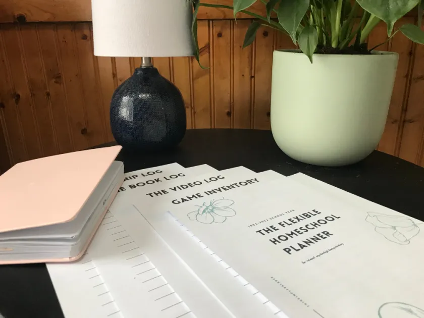 flexible homeschool planner pages printed on black table with lamp, plant, and book