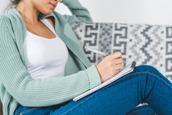 woman sitting on a couch, writing down in a spiral notebook what she learned from not buying clothes for a year