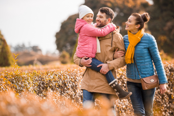 mom and dad carrying school-aged child through field in fall