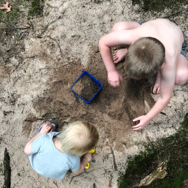 brother and toddler sister digging in sand together