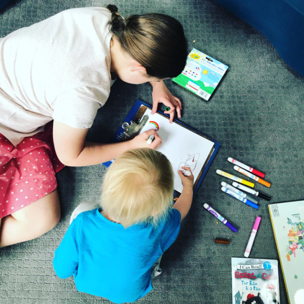 homeschooled sisters - one much older than the 2-year-old - drawing on the floor together