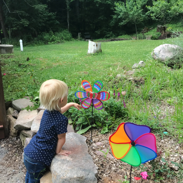 homeschooled two-year-old blond child looking at colorful spinner in a garden