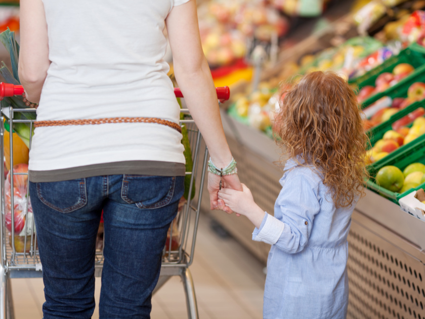 mom in grocery store with daughter, holding her hand while pushing the cart
