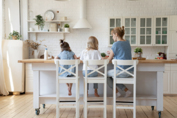 mom sitting at kitchen island with two daughters teaching them to cook