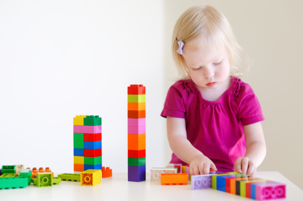 toddler building with colorful duplo blocks on white table