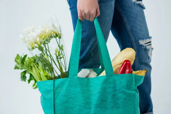 woman carrying reusable grocery bag full of flowers and vegetables