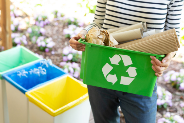 woman holding green recycling bin full of cardboard 