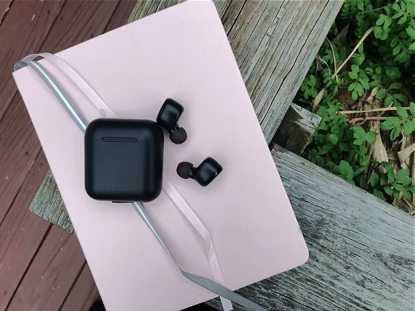 pink notebook with black wireless ear pods on top