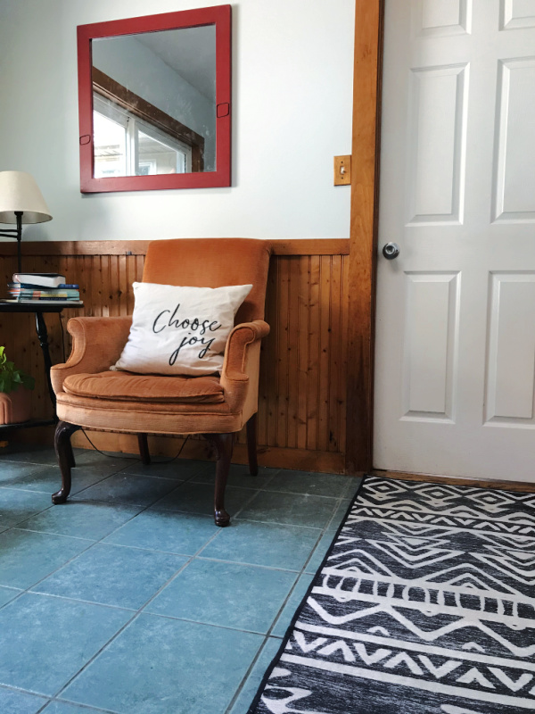 sunroom with orange chair, white canvas pillow saying, "Choose Joy" and black and white ruggable rug