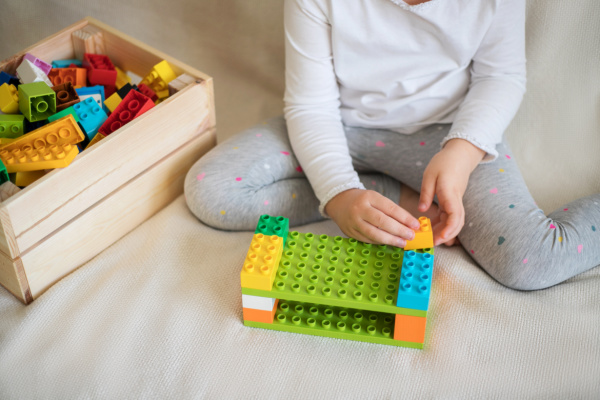 girl building with duplos, crate of blocks to her left